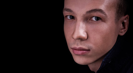 Close up portrait of a beautiful confident young man on a black isolated background in a Studio with copy space, he looks at the cameraの写真素材