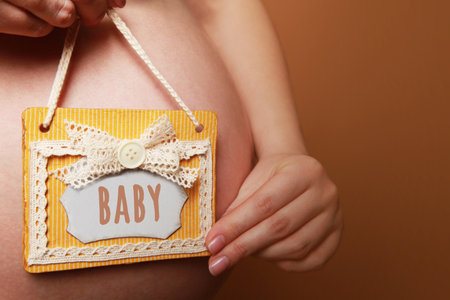 A pregnant woman holds a handmade sign with text baby next to her belly on a yellow backgroundの写真素材