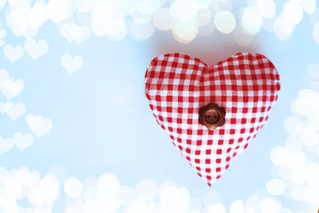 Handmade heart made of checkered fabric with a button flower in the middle on a blue background with...