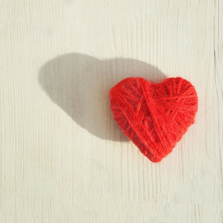 Red heart made of wool threads on a light wooden background. High quality photoの写真素材