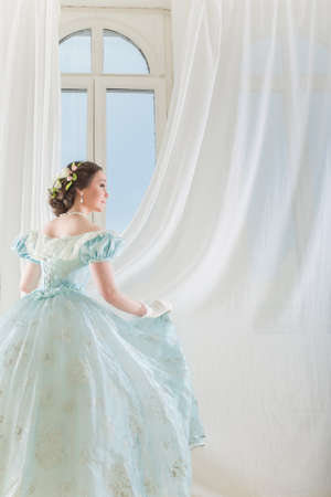 A beautiful elegant dark haired woman in a historic 1867 dress on background with window.の写真素材