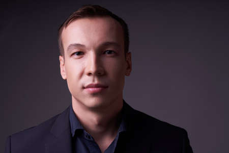 Close up portrait of a beautiful confident young business man on a black isolated background in a Studio with copy space, he looks at the cameraの写真素材