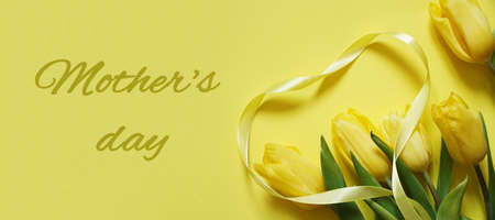 Five yellow fresh tulips on a yellow background with yellow heart made of ribbon, text Mother's dayの写真素材