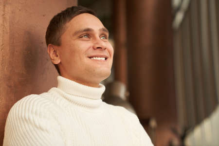 The handsome man in the room smiles and looks into the distance. A man in a white sweater. Copy space. High quality photoの写真素材