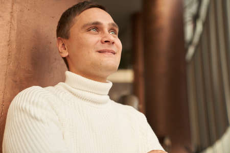 The handsome man in the room smiles and looks into the distance. A man in a white sweater. Copy space. High quality photoの写真素材