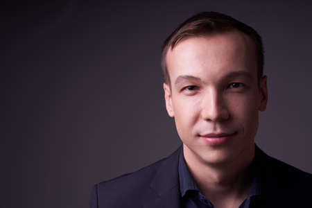 Close up portrait of a beautiful confident young business man on a black isolated background in a Studio with copy space, he looks at the cameraの写真素材