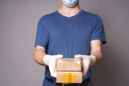 Hand of a white man in a medical mask and rubber gloves with two parcels on a gray background. Fast and safe delivery.の写真素材