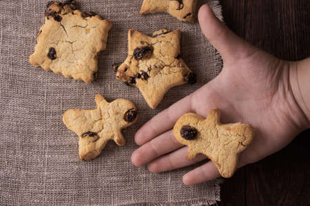 Homemade gluten-free, lactose-free cookies without sugar with raisins and chocolate on dark brown wooden background and Child hand holds gingerbreadの写真素材