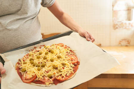 Pregnant woman holds on a baking sheet prepared for baking healthy gluten-free pizza with beef. Gluten-free cooking class. Cooking at home.の写真素材