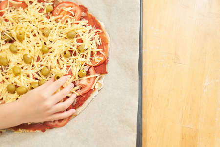 Childs hand with Pizza on baking paper prepared for baking. Healthy gluten-free pizza. Gluten-free cooking class. Photo with copy space.の写真素材