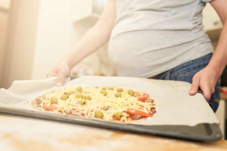 Pregnant woman holds on a baking sheet prepared for baking healthy gluten-free pizza with beef. Gluten-free cooking class. Cooking at home.の写真素材