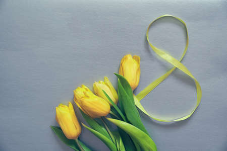 Five yellow fresh tulips on a grey background. Flowers with the number eight made of ribbon. Concept of holiday, March 8, International womans day. Vertical card with copy space.の写真素材