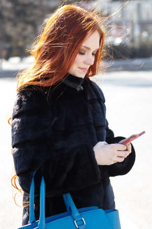 A beautiful unusual girl with red hair uses a mobile phone on the street,. High quality photoの写真素材