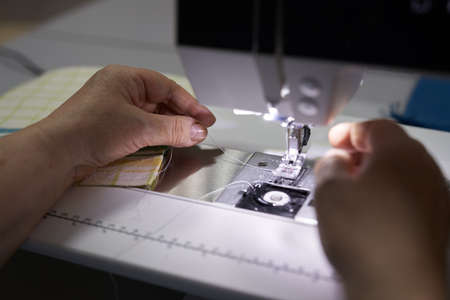 The workplace of a seamstress. The dressmaker works on a sewing machine. A tailor threads a thread into a sewing machine at his workplace. Hobby-sewing as a small business concept. High quality photoの写真素材