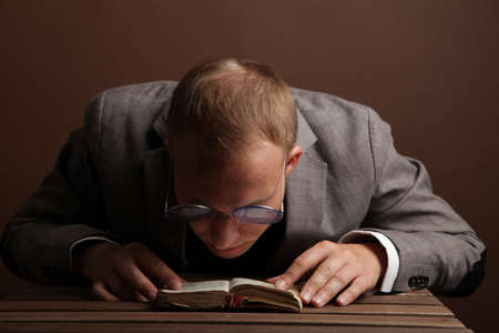 A handsome, confident businessman in a suit and round glasses, sitting isolated on a brown background, reading a book. A mans thoughtful, surprised face. High quality photoの写真素材