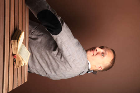Portrait of a man.A comical, cheerful, cheerful guy in a suit is sitting half-turned to the camera. The book is on the table. High quality photoの写真素材