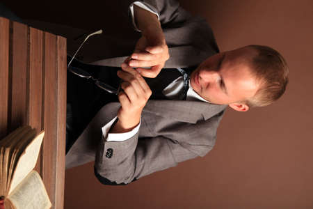 A confident businessman in a suit wipes round glasses, sitting alone on a brown background. The thoughtful face of a man. High quality photoの写真素材