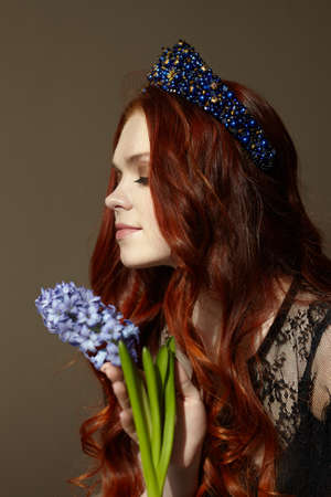 A red-haired woman with her eyes closed. Holds a blue hyacinth flower. On the head of the diadem is blue. High quality photoの写真素材