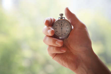 A mans hand holds a classic metal chrome mechanical analog stopwatch, on a defocused green background. High quality photoの写真素材