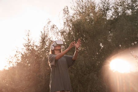 A girl wearing virtual reality glasses. He holds out his hands to the beam of sunlight. High quality photoの写真素材