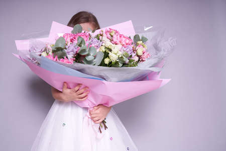 A girl in a white dress stands to the side and holds a bouquet of flowers, covering her face. Holiday concept. High quality photoの写真素材
