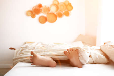 Close-up of a childs feet lying in bed in the morning, in the sunlight. High quality photoの写真素材