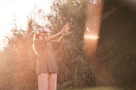 A girl holding a virtual reality helmet on her head with her hands. She holds out her hands to a ray of sunlight. High quality photoの写真素材