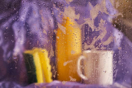 Close-up of household cleaning products and kitchen accessories. A plastic cup and a bottle with a...