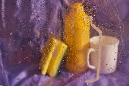 Household cleaning products and kitchen accessories. A plastic cup and a bottle with a sponge on a...