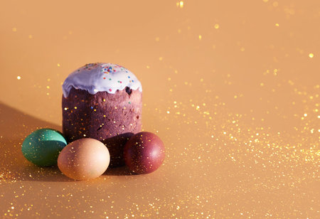 Colored Easter eggs and cake on a yellow background with a golden sheen. The background has space to...