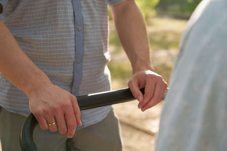 A young dad walking in the park with a baby in a stroller. Close-up of mens hands with a stroller....