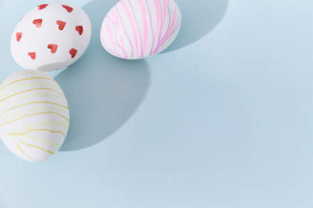 Close-up of three Easter eggs with a pattern of hearts and lines on a blue background. A shadow in...