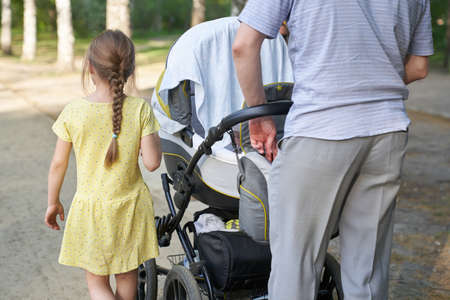 A man with a baby carriage and an older child is walking in a summer park. The concept of Fathers Day, a calm family atmosphere on a walk. High quality photoの写真素材