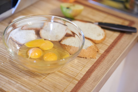 Three raw eggs in a clear glass bowl on the kitchen table with white bread. Step-by-step cooking of eggs for breakfast. High quality photoの写真素材