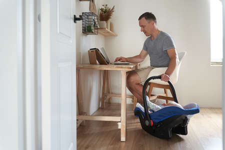 A handsome freelance man works on a modern laptop. A young father works at home and cradles his...