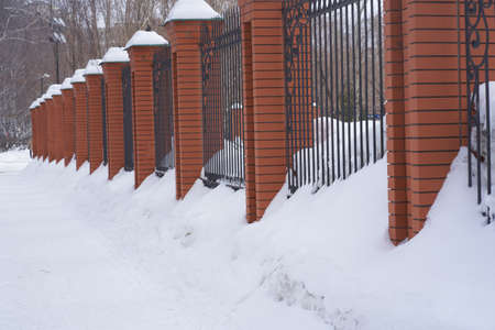 Metal fence with brick columns. Against the background of white snow on a winter day, traffic is difficult due to a large amount of snow. High quality photoの写真素材