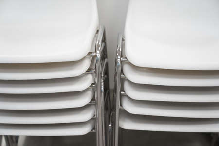 Close-up of white plastic chairs in a row waiting for visitors. White plastic chairs stand on top of each other against a white wall. High quality photoの写真素材