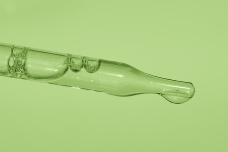 Pipette with liquid essence on a light green background. This is the consistency of micellar water. The concept of an extract for cosmetic and therapeutic purposes. High quality photoの写真素材