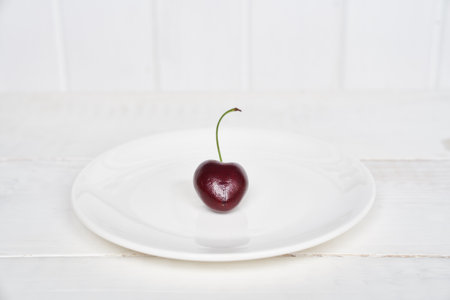 One heart-shaped cherry on a white plate. Ripe fresh juicy berry on a white background. Fruit background. valentines day. With space to copy. High quality photoの写真素材