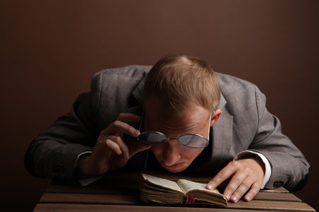Portrait of a man.A comical, cheerful, cheerful guy in a suit and glasses, holding a book in his hands, carefully examines the book. High quality photoの写真素材