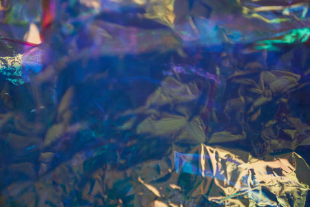 Holographic uneven, crumpled mother-of-pearl foil. Holographic iridescent abstract foil background. Unfocused background in blue tones. High quality photoの写真素材