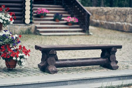 An old dark and low wooden bench on the background of a wooden ladder. There are pots of petunia flowers on the ladders. High quality photoの写真素材