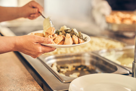 Close-up of a woman hands putting food on her plate, self-service in the dining room. High quality...