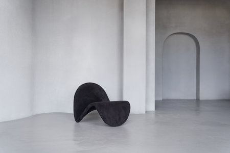 Modern interior with an elegant curved chair in black against a gray, rough, uneven wall with space...