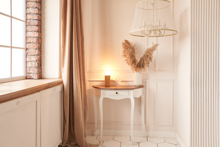 By the window there is a coffee table with a floor lamp and dried flowers in a vase. Interior design of a modern living room of a country house. High quality photoの写真素材