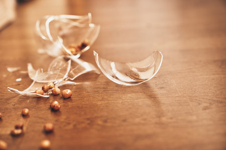 Close-up of a broken transparent glass of compote with raisins. Pieces of broken glass lie on the floor with space to copy. High quality photoの写真素材