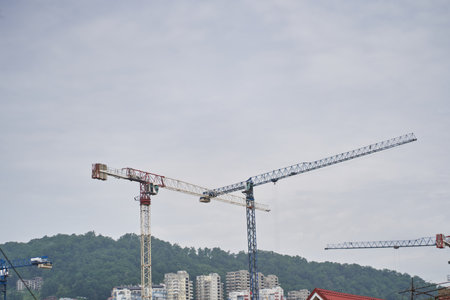 Construction crane and the upper part of the building with scaffolding on the background of the building under construction. Three tall construction cranes against a clear blue sky. High quality photoの写真素材