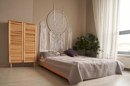 A dream catcher woven with the technique of knotted weaving, a macrame above the bed in the bedroom. Living room interior with space to copy. High quality photoの写真素材