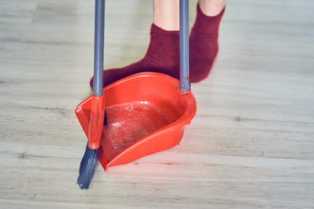 Close up of a plastic dustpan and red broom on the floor with womans legs. Cleaner, worker is using cleaning supplies. Background with copy space. Concept of cleaning home, dust, sweeping floor.の写真素材