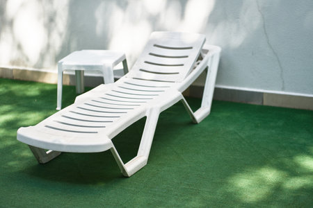 White plastic chair, chaise lounge on the grass with table. Background with copy space. Concept of...